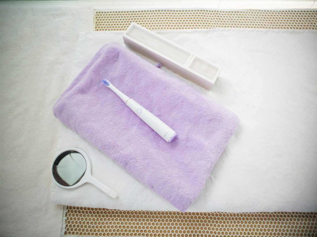 A lavender towel with an electric toothbrush and dental mirror laid out on a treatment bench