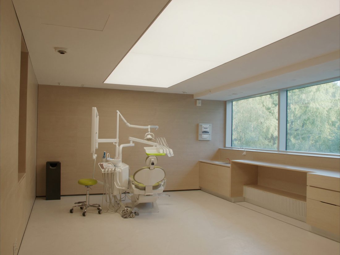 A treatment room with soft ceiling light and a wide window onto green trees
